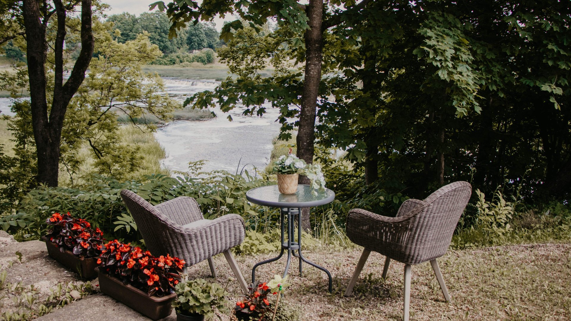 Two wicker chairs and a table on a terrace above the Venta, with Ventas Rumba waterfall beyond the trees