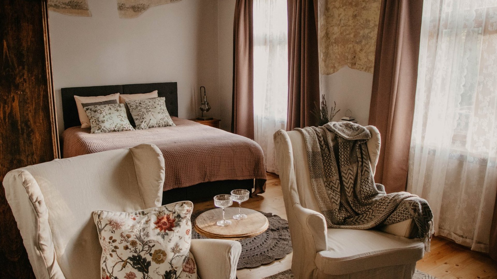 Bedroom with wing-back armchairs and tall curtained windows in the Taka apartment